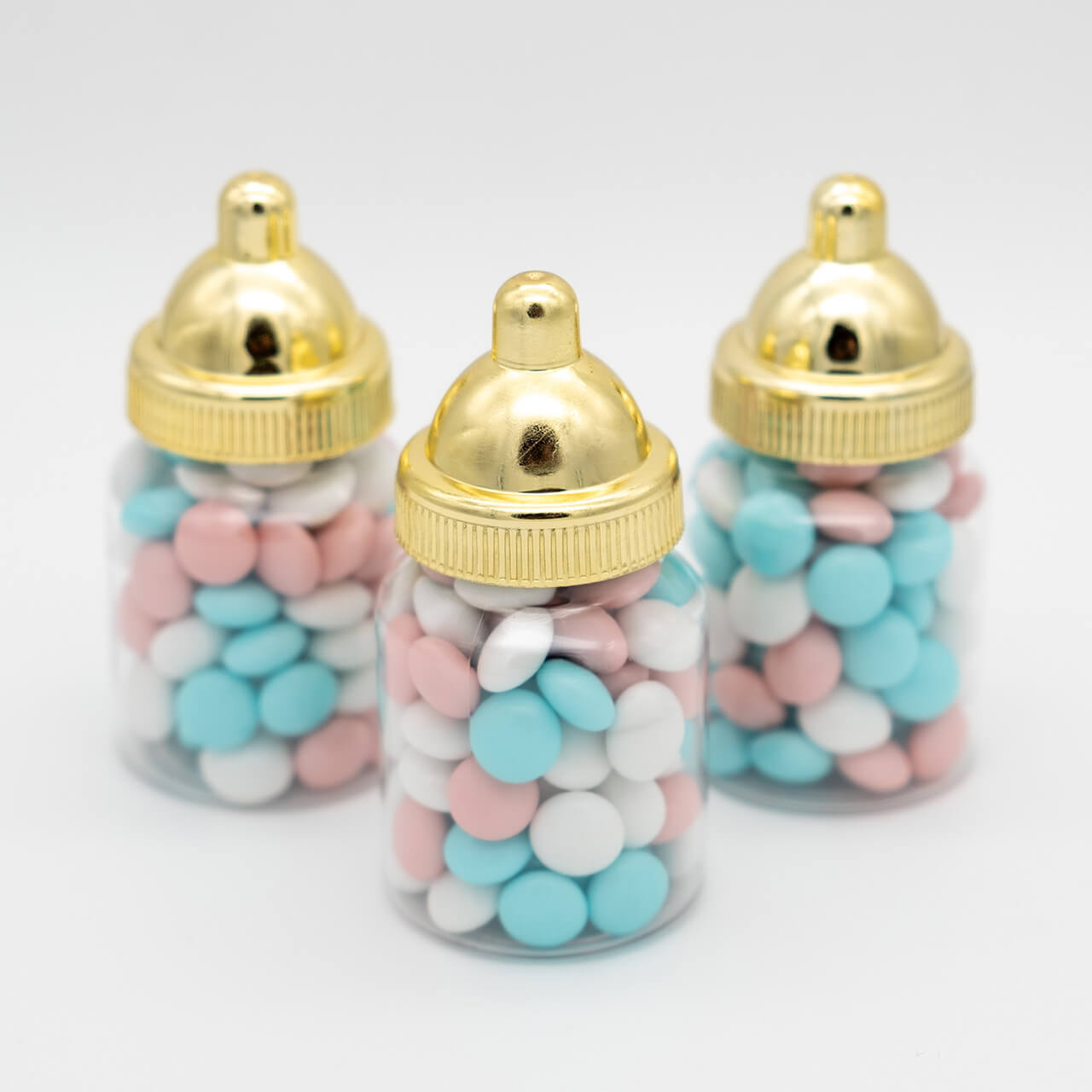 Drie babyflesjes met blauwe, roze en witte chocolade dragees en goudkleurige doppen